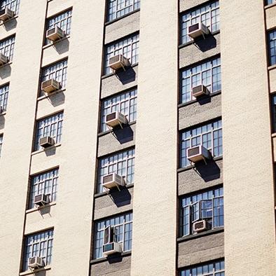 tan apartment building with air conditioning units coming out of most windows