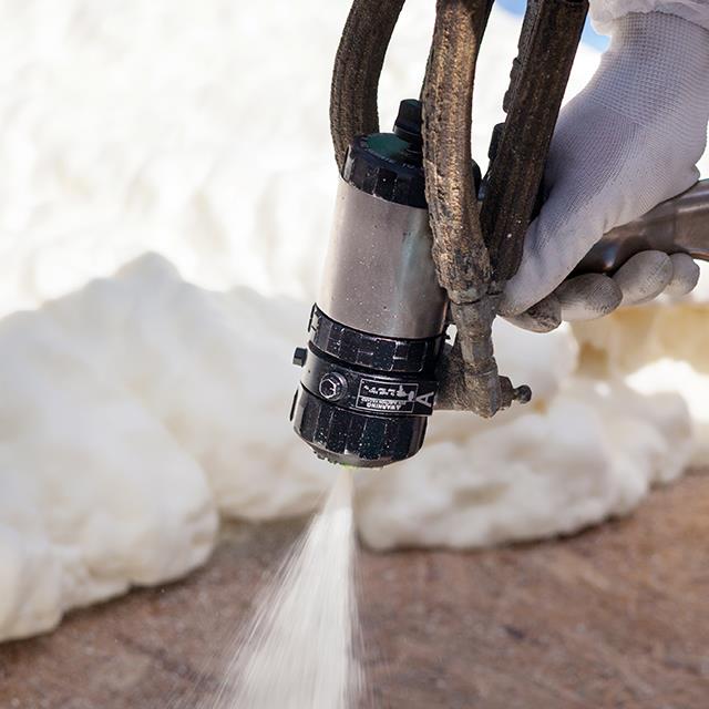 closeup of hand holding foam insulation sprayer spraying foam